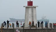 A cargo sails in the Taiwan Strait, behind tourists on a lighthouse on Pingtan island, the closest point to Taiwan, in China's southeast Fujian province on April 6, 2023. (Photo by GREG BAKER / AFP)