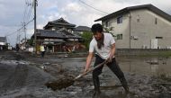 A man clears silt from a road following flooding in the city of Kurume, Fukuoka prefecture, on July 10, 2023, after heavy rains hit wide areas of Kyushu island. (Photo by Kazuhiro NOGI / AFP)
