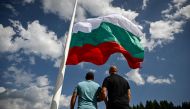 People watch the rising of a large Bulgarian flag during preparations ahead of the inauguration of an 111 m / 364 ft flagpole at Rozhen meadows near the city of Smolyan, some 80km south of Plovdiv, on July 13, 2023. (Photo by Nikolay Doychinov / AFP)