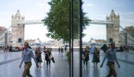 A man, reflected in a building, walks on the Southbank of the River Thames, with London Bridge on the background , central London, on August 14, 2023. Photo by HENRY NICHOLLS / AFP