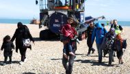 A man carrying a child in his arms, is followed by a migrant pregnant woman (2nd R), as they walk on the beach at Dungeness on the southeast coast of England, on August 16, 2023. (Photo by HENRY NICHOLLS / AFP)
 