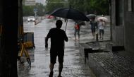 A man shelters from the rain with an umbrella in Beijing on July 30, 2023. (Photo by Pedro Pardo / AFP)

