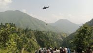 People watch as an army soldier slings down from a helicopter during a rescue mission to recover students stuck in a chairlift in Pashto village of mountainous Khyber Pakhtunkhwa province, on August 22, 2023. (Photo by AFP) 