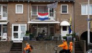 Cyclists dressed in orange ride past a house with a Dutch flag reading 