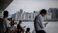People sit along a promenade next to Victoria harbour in Hong Kong on August 31, 2023, a day before the arrival of Typhoon Saola. (Photo by ISAAC LAWRENCE / AFP)