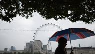 Pedestrians shelter from the rain beneath umbrellas while walking past the London landmark, the London Eye, from Embankment by the River Thames, in central London, on August 18, 2023 on a gloomy summer's day. Photo by HENRY NICHOLLS / AFP

