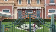 (FILES) In this file photo an employee cleans the grounds behind the closed gates of Disneyland Park on the first day of the closure of Disneyland and Disney California Adventure theme parks as fear of the spread of coronavirus continue, in Anaheim, California/

