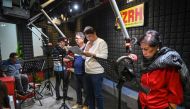This photo taken on July 17, 2023 shows Phil Cruz (3rd L), his brother Robert (2nd R) and other voice actors recording their part for a radio drama at a studio of a radio station in Manila. (Photo by Ted Aljibe / AFP)