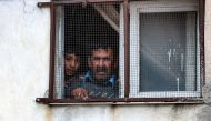 A man and a boy look out the window of a building at the scene where Palestinians were shot in the town of Azzun, east of Qalqilya in the occupied West Bank, on January 2, 2024. (Photo by Jaafar Ashtiyeh / AFP)