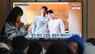 A woman walks past a television screen showing a news broadcast with a picture of Son Heung-min (L) and Lee Kang-in (R), at a railway station in Seoul on February 21, 2024. Photo by Jung Yeon-je / AFP