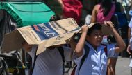 Students use a cardboard to protect themselves from the sun during a hot day in Manila on April 2, 2024. (Photo by Jam Sta Rosa / AFP)
