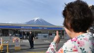 A person takes pictures of Mount Fuji from across the street of a convenience store, hours before the installation of a barrier to block the sight of Japan's Mount Fuji to deter badly behaved tourists, in the town of Fujikawaguchiko, Yamanashi prefecture on May 21, 2024. Photo by Kazuhiro NOGI / AFP