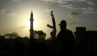 A fighter loyal to Sudan's army chief Abdel Fattah al-Burhan holds up a weapon backdropped by the minaret of a mosque, during a graduation ceremony in the southeastern Gedaref state on May 27, 2024. (Photo by AFP)