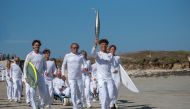 French surfer Louka Tirilly de Vera (centre) holds the Olympic flame flanked by members of the French Olympic surfing team as part of the Olympic Relay run in Plomeur, western France on June 7, 2024, ahead of the Paris 2024 Olympic and Paralympic Games. (Photo by Oscar Chuberre / AFP)