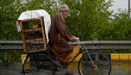A vendor carries chicks in a cage as he rides a bicycle along a street amid rainfall in Islamabad on June 5, 2024. Photo by Aamir QURESHI / AFP.