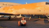 A handout picture released by the Just Stop Oil climate campaign group shows an activist sitting in front of a plane after spraying orange paint on private jets at Stansted Airport, northeast of London, on June 20, 2024. (Photo by Handout / Just Stop Oil / AFP) 