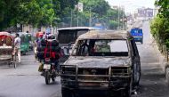 Commuters drive past a burnt car after students set it on fire amid the ongoing anti-quota protest in Dhaka on July 19, 2024. (Photo by Munir UZ ZAMAN / AFP)
