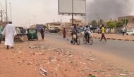 Smoke rises above buildings as people walk along a street in Omdurman City in Sudan on July 15, 2023. (Photo by AFP)

