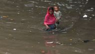 A woman with her child wade through a flooded street amid heavy rainfall in Lahore on August 1, 2024. (Photo by Arif Ali / AFP)
