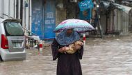 A woman carries her infant as she wades through a flooded street during heavy rainfall in Lahore on August 1, 2024. (Photo by Syed Murtaza / AFP)

