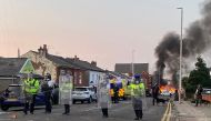 Smoke billows from a fire started by protesters as riot police stand guard after disturbances in Southport, northwest England, on July 30, 2024, a day after a deadly child knife attack. Photo by Roland LLOYD PARRY / AFP