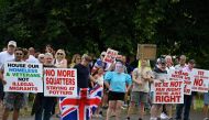 Protesters, including one wearing a mask of Britain's Prime Minister Keir Starmer, hold placards during a 'Enough is Enough' demonstration called by far-right activists near a hotel housing asylum seekers in Aldershot on August 4, 2024.  (Photo by Justin Tallis / AFP)