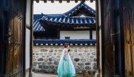 A woman wearing a traditional dress walks past a doorway at Namsangol Hanok Village in Seoul on August 8, 2024. (Photo by ANTHONY WALLACE / AFP)
