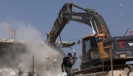 A member of the Israeli security forces walks past a bulldozer demolishing a house belonging to Palestinians, located in the area C, which lies under Israel's military control since 1967, in Yatta village in the southern area of the occupied West Bank, on November 6, 2024. (Photo by HAZEM BADER / AFP)
