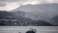 This photograph shows a sinked boat and in background damages and smoke on hills near the city of Mamoudzou, on the French Indian Ocean territory of Mayotte, on December 17, 2024, after the cyclone Chido hit the archipelago. (Photo by Dimitar Dilkoff / AFP)