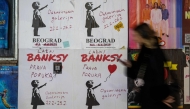 A woman walks past a poster advertising a gallery where an alternative and free exhibition showcases the work of the famous elusive artist Banksy in Belgrade on February 25, 2025. Photo by Andrej ISAKOVIC / AFP