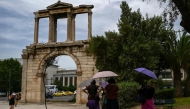 (FILES) Tourists holding umbrellas walk in front of the ancient Roman Andrian Gate, during a hot day in Athens on June 13, 2024. (Photo by Aris MESSINIS / AFP)

