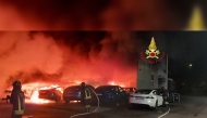 This handout image taken and released on March 31, 2025, by the Vigili del Fuoco, the Italian Corps of Firefighters, shows firefighters working to put out a fire at a Tesla dealership, in which 17 cars were destroyed or seriously damaged, in Torrenova, on the outskirts of Rome. (Photo by Handout / Vigili del Fuoco / AFP) 
