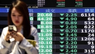 A woman walks past screens displaying average stock prices at the Taiwan Stock Exchange in Taipei on April 7, 2025. (Photo by I-Hwa Cheng / AFP)