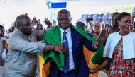 Gabon's junta chief Brice Oligui Nguema is draped with a Gabon flag while standing next to his wife Zita Nyangue Oligui Nguema as they celebrate him winning the presidential election, at his election campaign headquarters in Libreville on April 13, 2025. G(Photo by Daniel Beloumou Olomo / AFP)