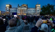 People watch the Reichstag building illuminated in a tribute to the artwork of artists Christo and Jeanne-Claude, in Berlin on June 9, 2025. (Photo by Odd Andersen / AFP)