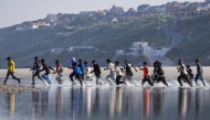 Migrants rush to try to board a smuggler's boat in an attempt to cross the English Channel on the beach of Equihen, northern France, on June 30, 2025. (Photo by Sameer Al-DOUMY / AFP)
