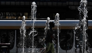 A man walks through the water jets of a public fountain as outside temperatures reach 37 degrees celsius in Brussels on July 1, 2025. Photo by Nicolas TUCAT / AFP