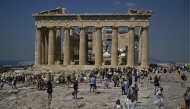 Tourists walk in front of the Parthenon Temple as they visit the Acropolis archaeological site in Athens on June 14, 2023. Photo by Louisa GOULIAMAKI / AFP