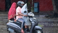 A schoolboy covered in a plastic sheet clings to an elder driving a scooter amid rainfall in India on July 16, 2025. (Photo by AFP)

