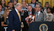 US President Donald Trump (L) looks at a photo as a man who lost his son to fentanyl speaks before the signing of the 