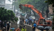 Rescuers and people look as a crane removes the wreckage of a van from a drainage after heavy monsoon rains in Islamabad on July 21, 2025. (Photo by M ASIM KHAN / AFP)