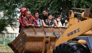 Residents ride on a front loader to cross a flooded street after heavy rains at Taishitun village in Miyun district, on the outskirts of Beijing on July 28, 2025. Photo by Jade GAO / AFP