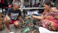 This photo taken on June 26, 2025 shows Dexter Barsigan (L), who had developed health issues after years of dismantling scavenged electronic waste, crouching beside his wife Rosalie Sedantes as she prepares to strip parts from discarded electronic equipment in Manila. (Photo by Ted ALJIBE / AFP)