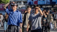 People shield their eyes from the sun as they cross Shibuya crossing on a hot day in Tokyo on July 26, 2025. (Photo by Yuichi YAMAZAKI / AFP)
