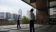 Men relax under an office building in Beijing’s central business district on July 31, 2025. (Photo by GREG BAKER / AFP)