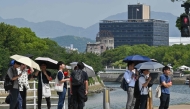 A group of tourists shelter under umbrellas in the summer heat as they wait for the light to change, with the Atomic Bomb Dome in the background in downtown Hiroshima on August 5, 2025. (Photo by Richard A. Brooks / AFP)