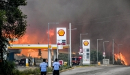 Inhabitants stand on a road as a wildfire approaches a gas station near the city of Patras, western Greece on August 12, 2025. (Photo by Eurokinissi / AFP) 