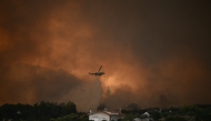 A firefighting helicopter drops water over a wildfire near the city of Patras, western Greece on August 13, 2025. Greece on August 13, 2025 battled to contain more than 20 wildfires including one menacing its third-largest city Patras as a heatwave stoked blazes and forced the evacuation of thousands in southern Europe. (Photo by Aris MESSINIS / AFP)
