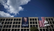 Workers hang a large photo of US President Donald Trump next to a US flag on the facade of the Department of Labor headquarters building in Washington, DC, on August 27, 2025. (Photo by Drew Angerer / AFP)