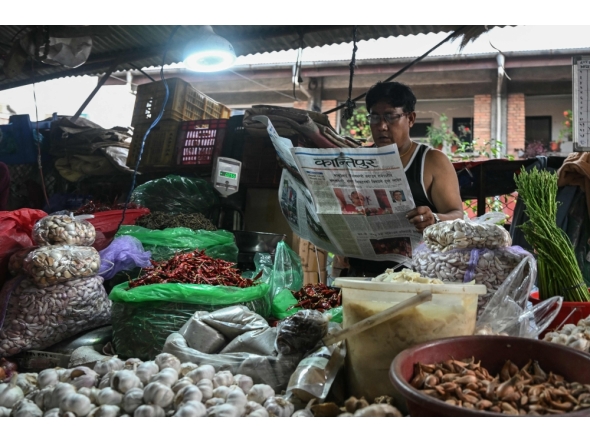 A vegetable vendor reads a Nepali-language newspaper on a roadside in Kathmandu on September 12, 2025. (Photo by Arun Sankar / AFP)
 
